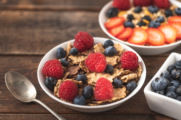 Granola chips with blueberries and raspberries in white bowl in dark wooden desk.