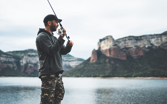 fisherman enjoy hobby with fishing rod on lake, person catch fish on background mountain, holiday relaxation fishery concept