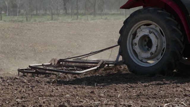 Footage of a tractor aligning the earthy surface on a field with a spike tooth harrow and preparing it for sowing