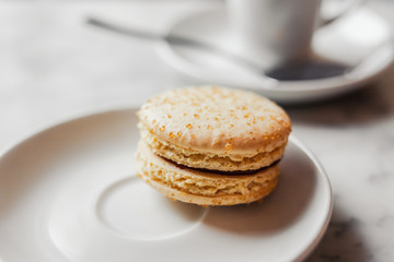 Obraz na płótnie Canvas Close up photo of macaron with salted caramel on a white saucer with blurred cup of coffee on the background