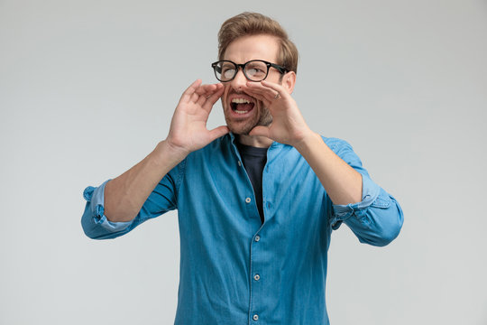 angry young casual man holding hand to mouth and shouthing