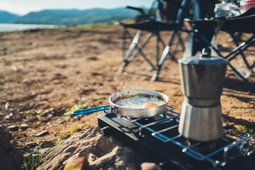 person cooking fried eggs hot drink in nature camping outdoor, cooker prepare scrambled omelette breakfast picnic, tourism recreation outside; campsite lifestyle