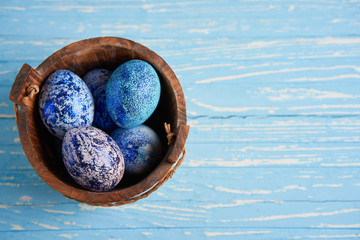 Blue cosmos chicken eggs lie in round wooden basket which stands on a blue wooden table.