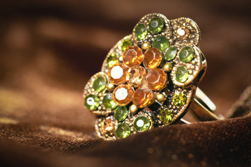 Old golden color ring with artificial gemstones on brown velvet cloth background close up.
