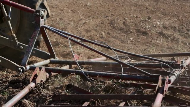 Slow motion footage of a tractor aligning the earthy surface on a field with a spike tooth harrow and preparing it for sowing