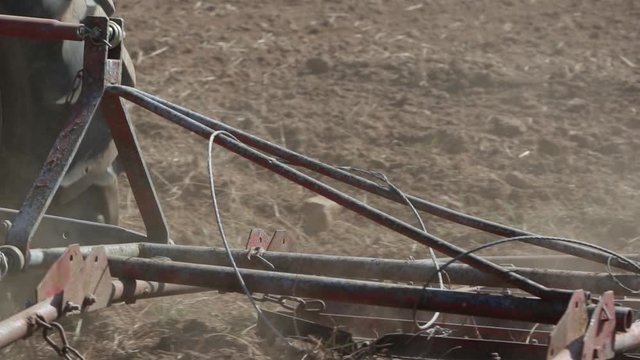 Slow motion footage of a tractor aligning the earthy surface on a field with a spike tooth harrow and preparing it for sowing