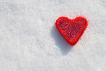 Red heart in sparkles on a white snow background.