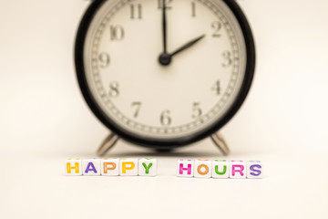 "Happy Hours" is written by cubes with letters with a black and white classic alarm clock on white background