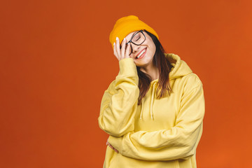 People, youth, leisure and lifestyle concept. Fashionable beautiful young Caucasian young female student laughing, having rest at home after lectures at college. Isolated over orange.