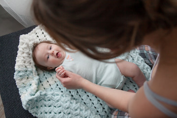 Top view of the 3 month baby lying in his back on blanket. The back of the mother look to newborn baby and holding the hands of infant.