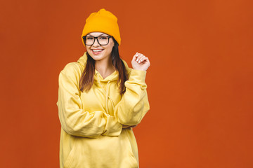 People, youth, leisure and lifestyle concept. Fashionable beautiful young Caucasian young female student wearing stylish clothing laughing, pointing finger. Isolated over orange. 