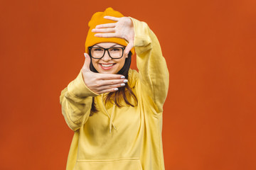 People, youth, leisure and lifestyle concept. Fashionable beautiful young Caucasian young female student wearing stylish clothing laughing, pointing finger. Isolated over orange.