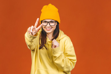 People, youth, leisure and lifestyle concept. Fashionable beautiful young Caucasian young female student wearing stylish clothing laughing, pointing finger. Isolated over orange.