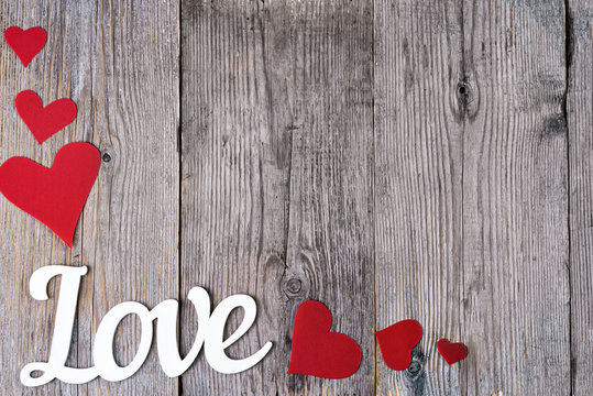 The word Love is written on a gray wooden background next to the red hearts in the lower left corner of the image. Focus Offset. Place for text in the middle of the frame.