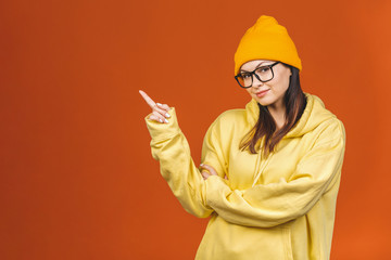 People, youth, leisure and lifestyle concept. Fashionable beautiful young Caucasian young female student wearing stylish clothing laughing, pointing finger. Isolated over orange.