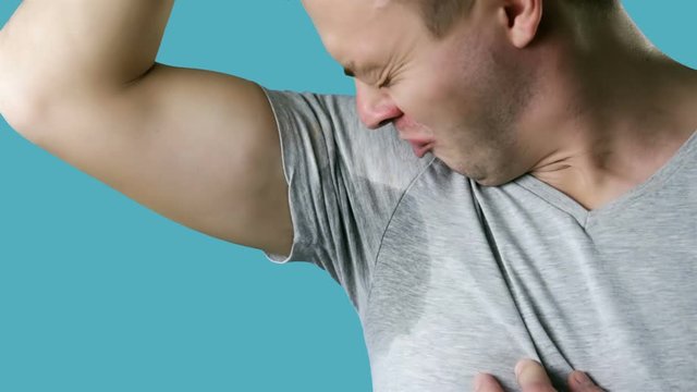 Young man is worried and shows sweating stain problem with sweating. Bad smells concept.