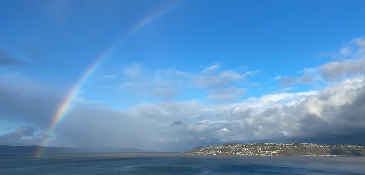 Panorama picture of rainbow in stormy sky over Tacoma Washington and Puget Sound