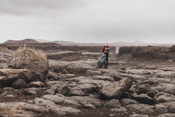 Couple in love walking and kissing in Iceland. Stone volcanic desert around, in the middle of nowhere. Dramatic nordic landscape, cold weather. Wearing in traditional wool sweaters, jeans and skirt.