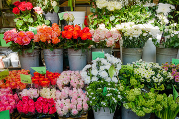 Fototapeta na wymiar Front view of colourful various bouquet of roses and flowers in metal vases on shelf in front of flower stall or floral shop at farmer market in Europe. Typical atmosphere of flower store. 