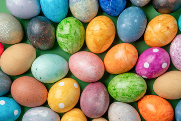 Different easter eggs with straw on wooden plate on green table