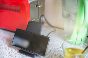smartphone wireless charging on charging stand next to tea glass cup on kitchen tabletop