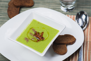 Green vegetarian broccoli cream soup with rye crackers on a wooden table in a restaurant or cafe.