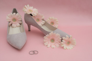 wedding concept. gerbera flowers, rings, beige shoes on a pink background.