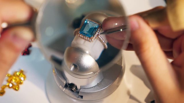 Jeweller, goldsmith uses loupe and tool while working with a ring at a jewellery workshop.