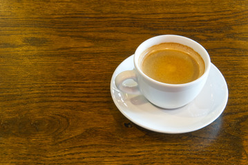 Cup of coffee on wooden table in restoran or coffee house. White ceramic cup view above with copy space