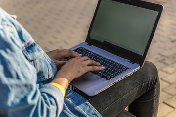 Fototapeta premium View of the hands of a woman typing on her laptop sitting on a park bench