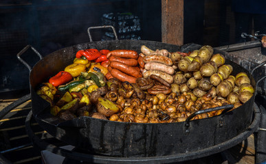 Frying pan with fried potatoes, sausages, mushrooms and pepper.Street food and outdoor cooking concept.