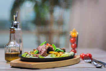 Fried pieces of meat with vegetables in a hot pan on a wooden table in a restaurant.