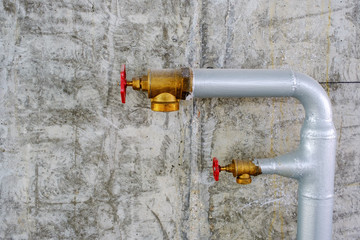 Two metal water pipes of industrial extinguisher system with brass valves on grey concrete wall...