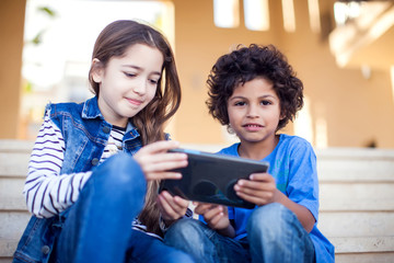Two kids boy and girl playing with tablet outdoor. Children and gadget addiction concept