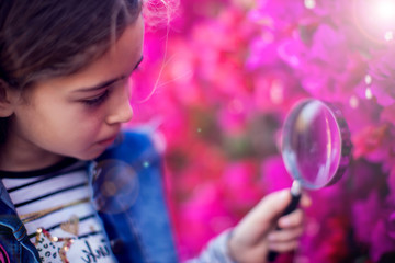 Fototapeta na wymiar A kid girl looking through magnifier at plants. Children, discovery and botany concept