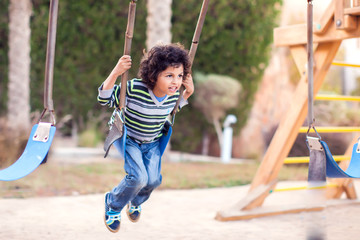 A smiling kid boy on a swing. Childhood and activity concept