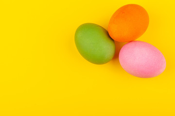 Colorful handmade Easter eggs. Top view of three eggs. Isolated on a yellow background. Preparing for Easter.