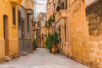 Fototapeta na wymiar Old medieval street with yellow buildings and flower pots in Birgu, Valletta, Malta
