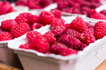 Raspberries in a cardboard bio eco recycled container on a market counter. Bright juicy berries. Selective focus