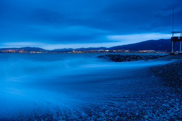 Gelendzhik beach in the evening in a storm. The waves at high speed turn into a blue fog. Pebble beach, breakwater. In the background, the Caucasus mountains, city of Gelendzhik