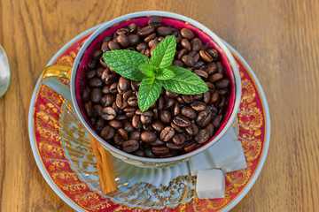 Vintage cup full of coffee beans and mint leaves