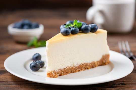 Cheesecake slice with blueberries on white plate, wooden table background. Tasty Sweet dessert. Classical New York Cheesecake