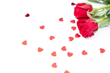 Two red roses on a white surface with heart shape confetti