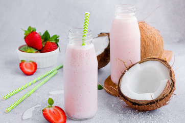 Strawberry coconut smoothie on coconut milk in a glass jar with a straw on a gray background. Healthy food concept. Horizontal orientation