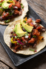 Mexican pork chorizo tacos with avocado and beans on wooden background