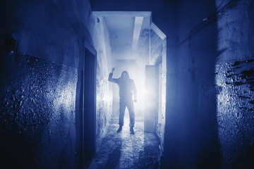 Dangerous Murderer or killer with Knife in hand and light from back in scary corridor in Phantom Blue color toned.