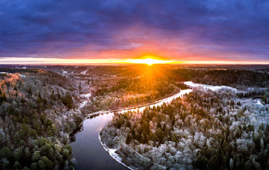 Stunning sunrise over valley surrounded with forest and river covered in snow. Scenic aerial landscape.