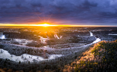 Stunning sunrise over valley surrounded with forest and river covered in snow. Scenic aerial landscape.