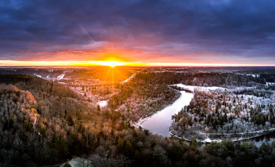 Stunning sunrise over valley surrounded with forest and river covered in snow. Scenic aerial landscape.