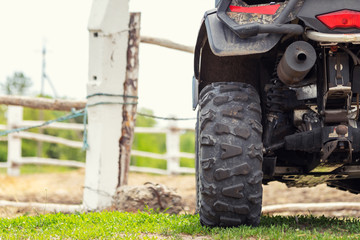 ATV quad bike vehicle standing near wooden fence at farm or horse stable. Back view of all wheel...